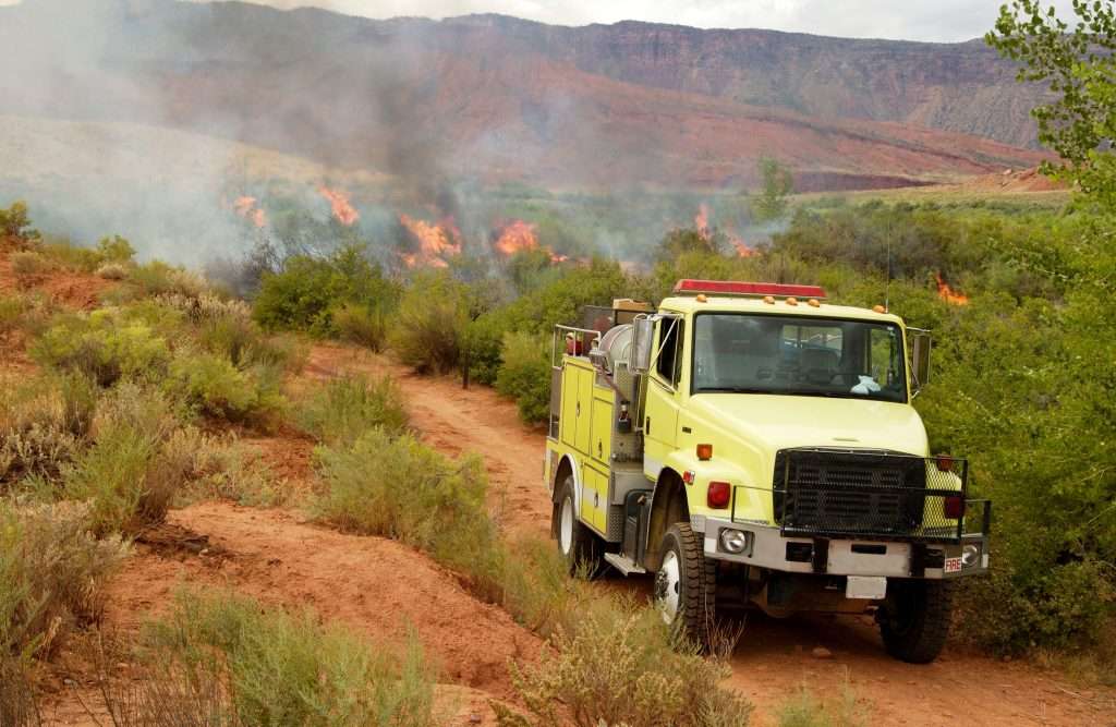 A lime yellow Type 3 fire apparatus navigating a dirt road toward an active brush fire, representing the used wildland apparatus available at Bradford Fire Apparatus
