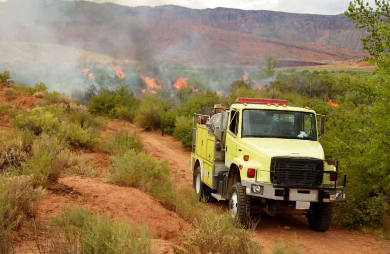 A lime yellow Type 3 fire apparatus navigating a dirt road toward an active brush fire, representing the used wildland apparatus available at Bradford Fire Apparatus